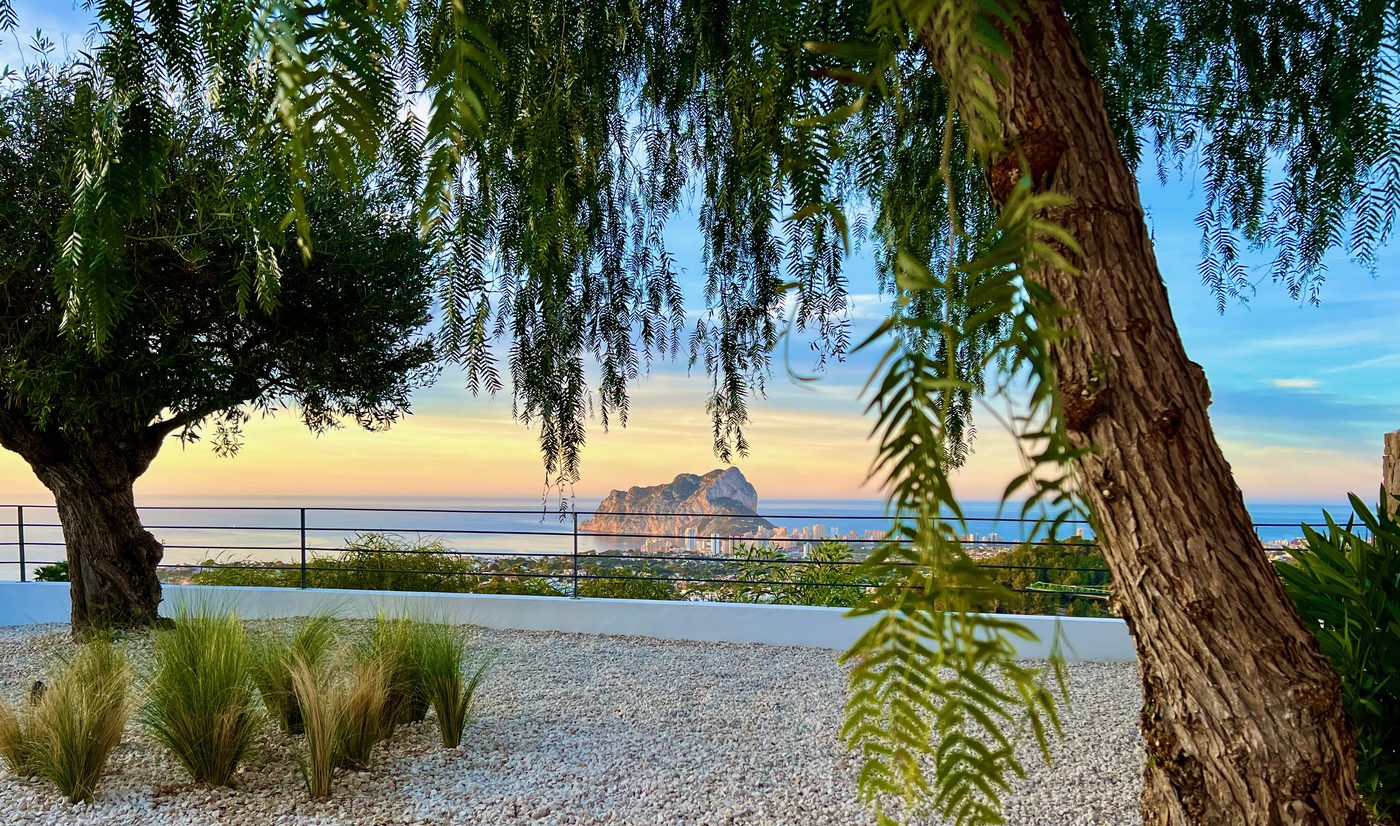 Garden terrace with Peñón de Ifach silhouetted at sunset through olive trees